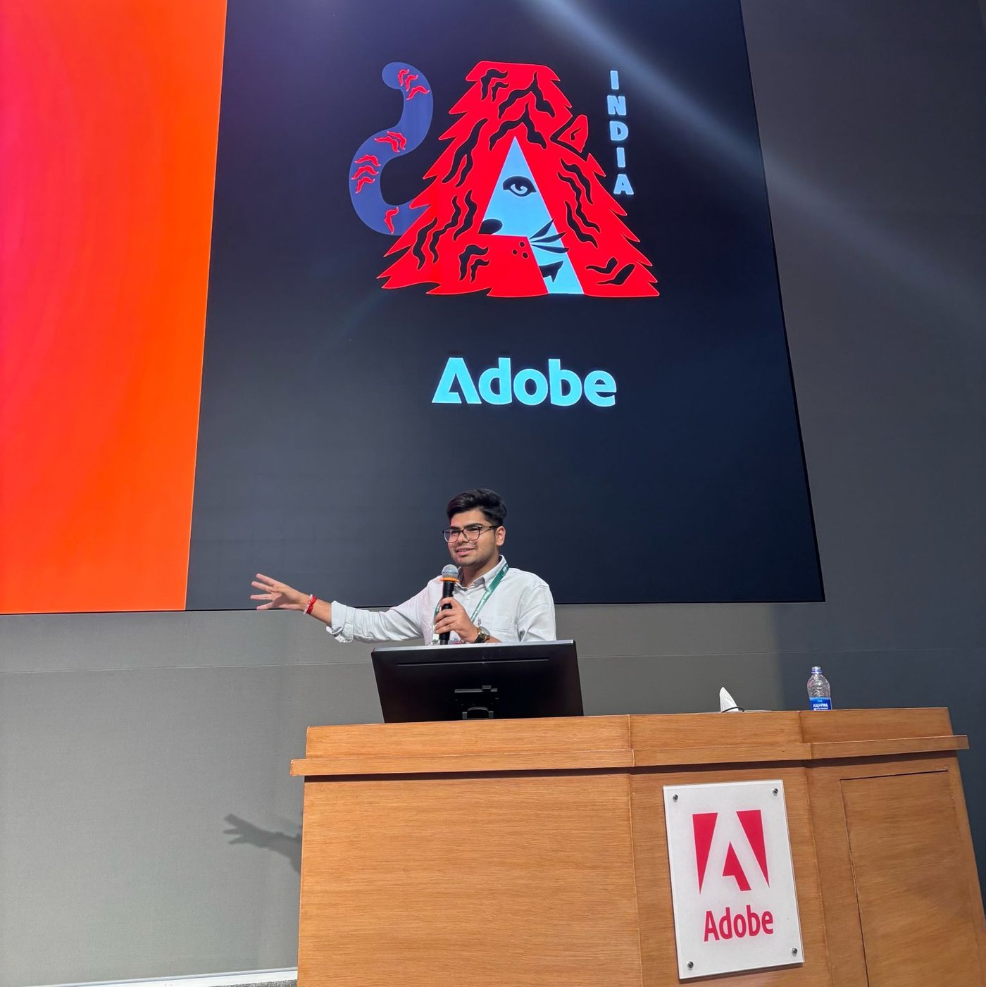 Shaswat Naman speaking on stage at the Adobe Education Summit in Noida, in front of the Adobe India graphic